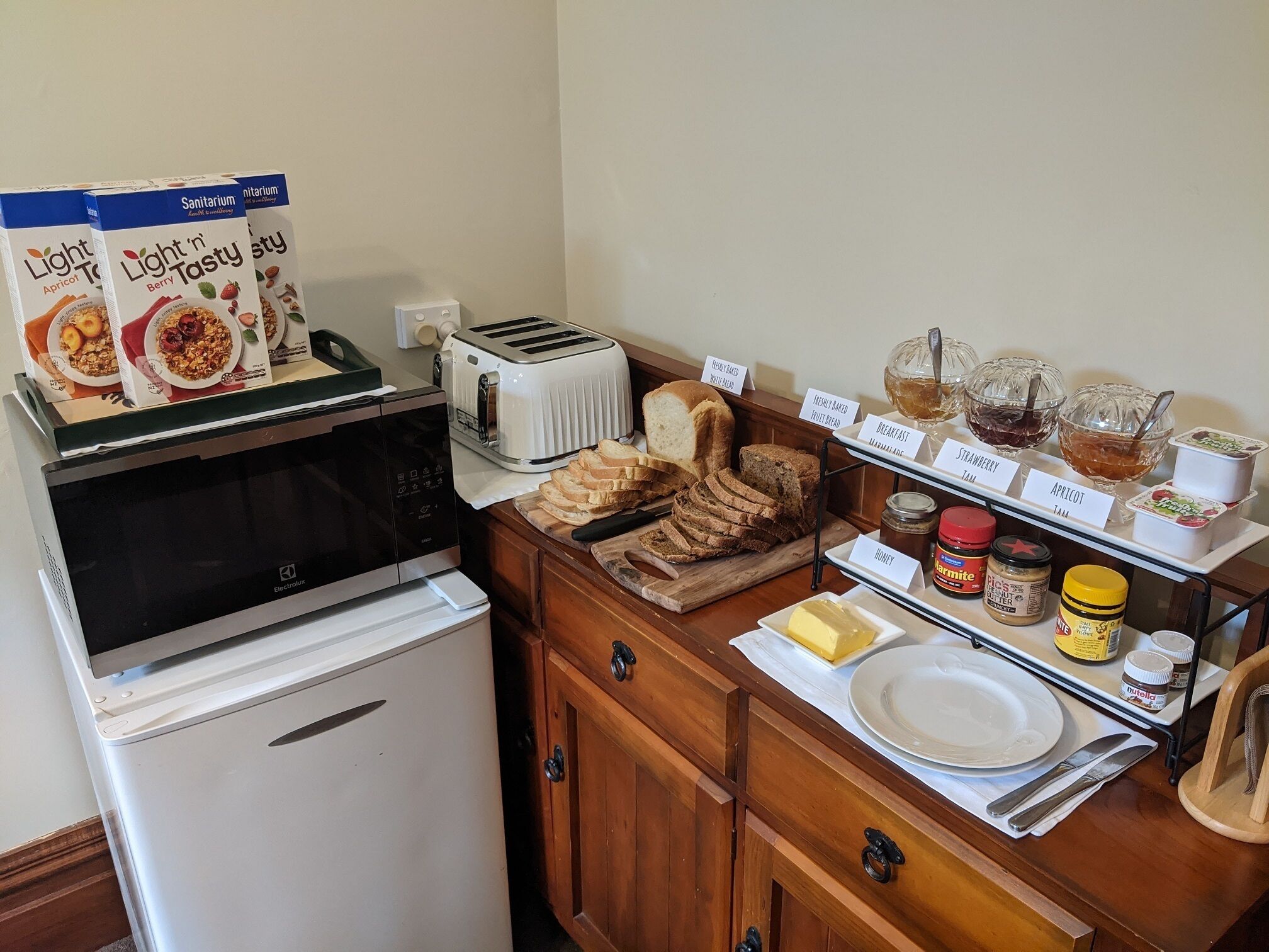 A kitchenette with a toaster, a refrigerator, a cutting board with bread, and various breakfast items like jam and honey.
