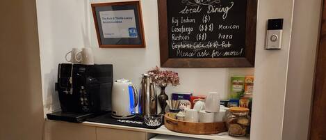 Een kleine keuken met een koffiezetapparaat, een koelkast en een krijtbord waarop lokale eetgelegenheden staan.