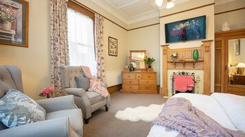 A well-furnished bedroom with a bed, two armchairs, a dresser, and a television displaying 'The Bad Seed'.