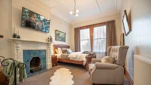 A bedroom with a fireplace, a bed, a chair, a television, and a large window with curtains. - The Fern & Thistle Boutique Accommodation - Drinks, Hotpool, Sauna (Benhar)