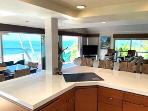 A modern kitchen with a large island, a dining area with a view of the ocean, and a living area with comfortable seating.