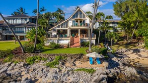 A two-story house with a balcony, surrounded by tropical vegetation and a rocky beach. - 3br/3.5ba Oceanfront home with pool and hot tub! (Lahaina)