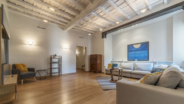 Amplia sala de estar con piso de madera, un sofá, una mesa de centro y una estantería.