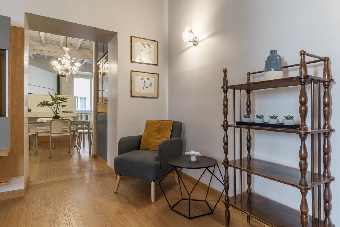 Ein modernes Wohnzimmer mit Holzboden, einem grauen Sessel, einem kleinen runden Tisch und einer Holzregalanlage mit Dekorationen.