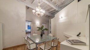 Un comedor moderno con una mesa de vidrio, sillas de mimbre, una araña y una pared blanca con un libro y una escultura de pájaro.