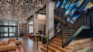 A spacious lobby with a modern staircase, a leather sofa, and a large chandelier. - The Gordon Hotel (Eugene)