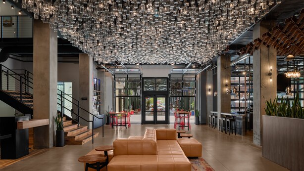 A modern lobby with a large leather sofa, a patterned rug, and a ceiling of hanging glass bottles. - The Gordon Hotel (Eugene)