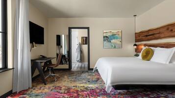 A hotel room with a large bed, a desk with a chair, a television, and a colorful carpet.