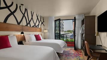 A hotel room with two beds, a desk, a chair, a colorful carpet, and a view of the city.