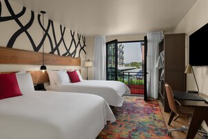 Habitación de hotel con dos camas, un escritorio, una silla, una alfombra colorida y vistas a la ciudad.