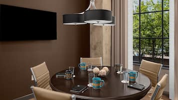 A round dining table with six chairs, a modern pendant light, and a large window with a view of trees.