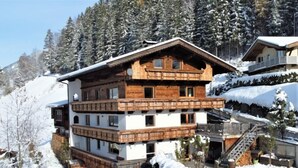 Una cabaña de madera de varios pisos con balcones, rodeada de árboles cubiertos de nieve y un paisaje montañoso.