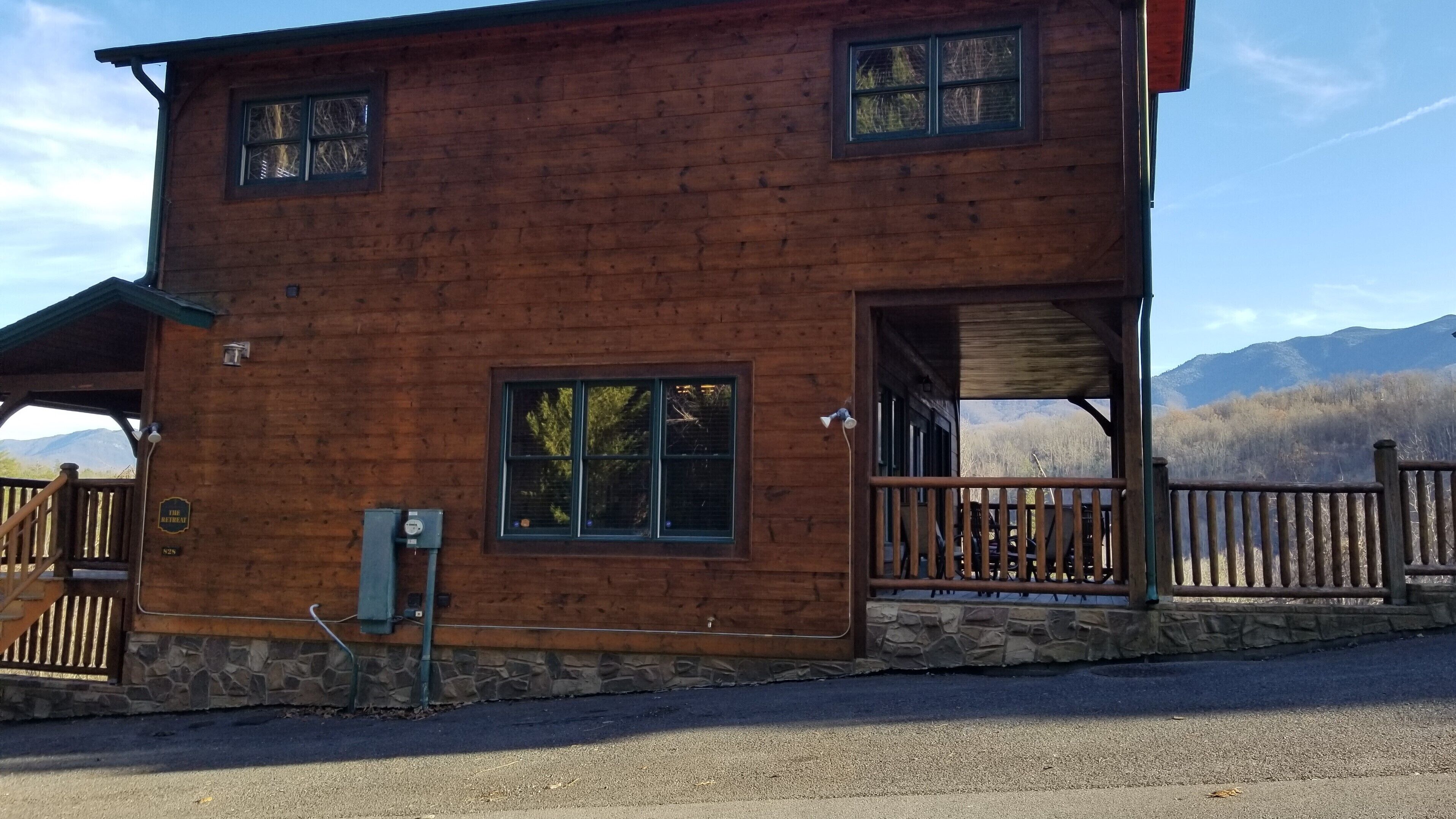 A wooden cabin with a stone foundation, a porch with a railing, and a view of mountains in the background.