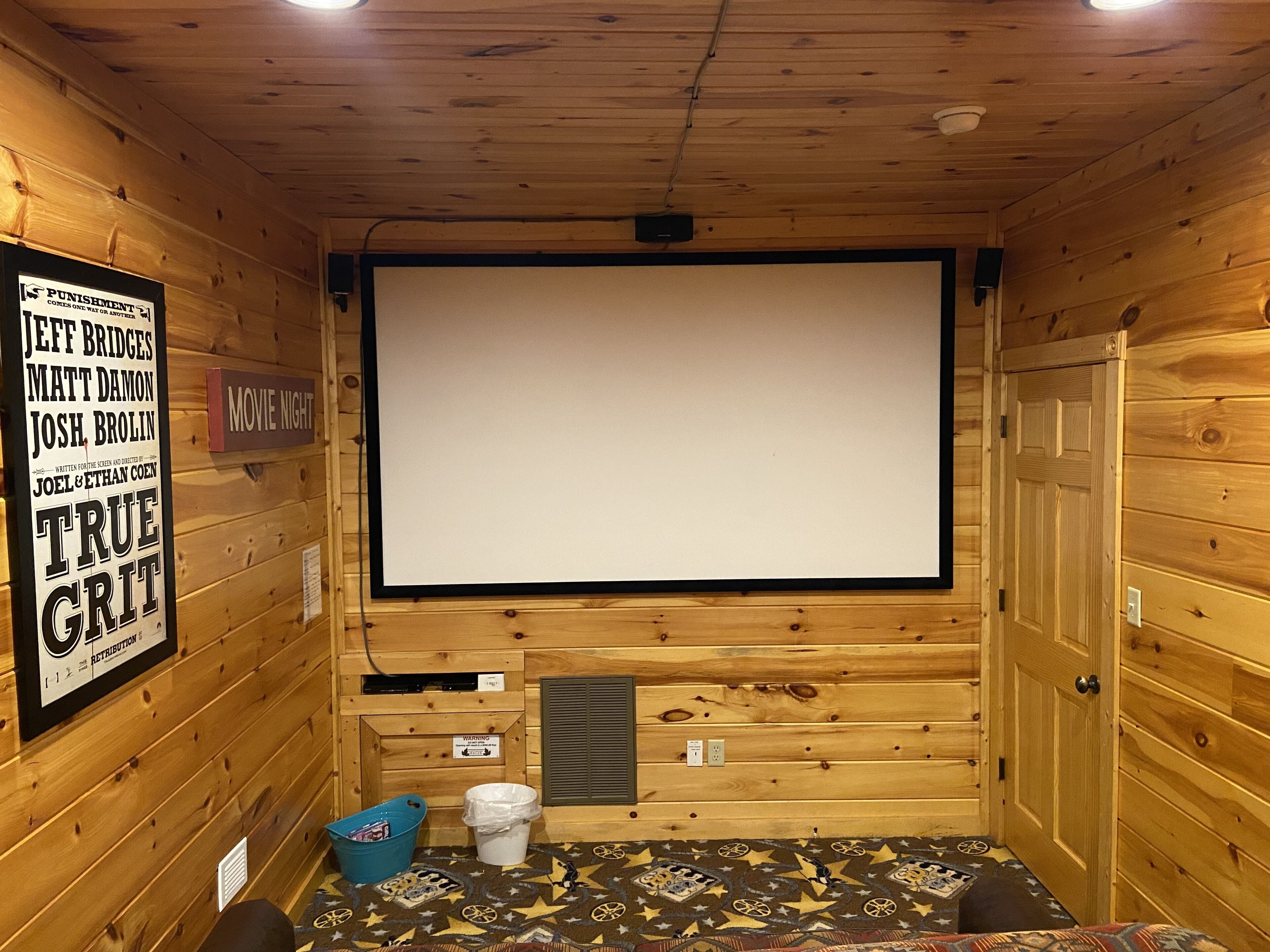 Une petite pièce aux murs lambrissés, équipée d’un grand écran pour les soirées cinéma, d’un projecteur et d’une console de commande pour le projecteur.