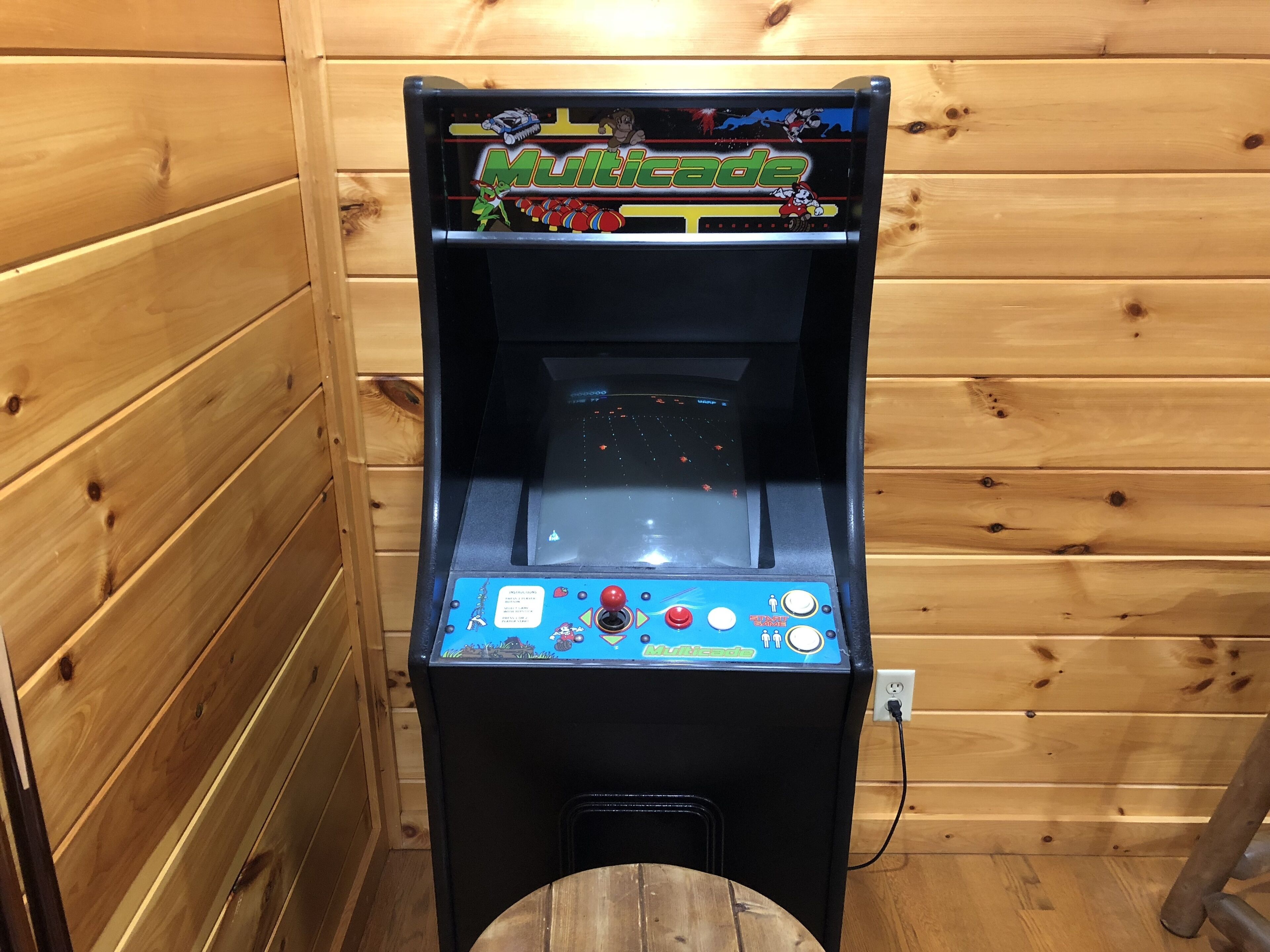 Máquina de videojuegos con joystick y botones, frente a una pared de madera.