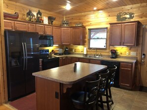 A kitchen with wooden cabinets, a refrigerator, a microwave, a coffee maker, and a window with blinds. - Mnt Views Hot Tub Theater & Game En-Suites 7 Min DT (Gatlinburg)