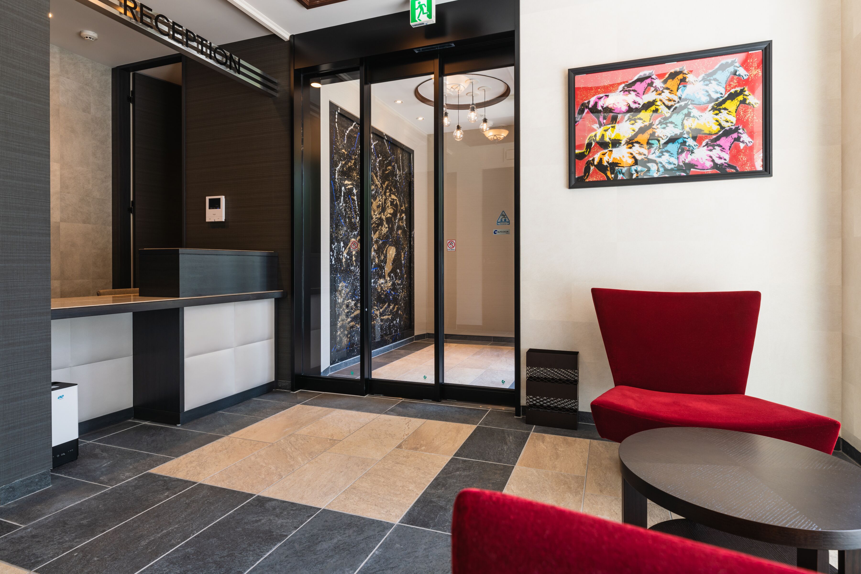 A reception area with a reception desk, a red chair, a glass door leading to a hallway, and a colorful abstract painting on the wall.