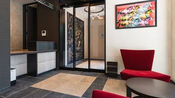 A reception area with a reception desk, a red chair, a glass door leading to a hallway, and a colorful abstract painting on the wall.