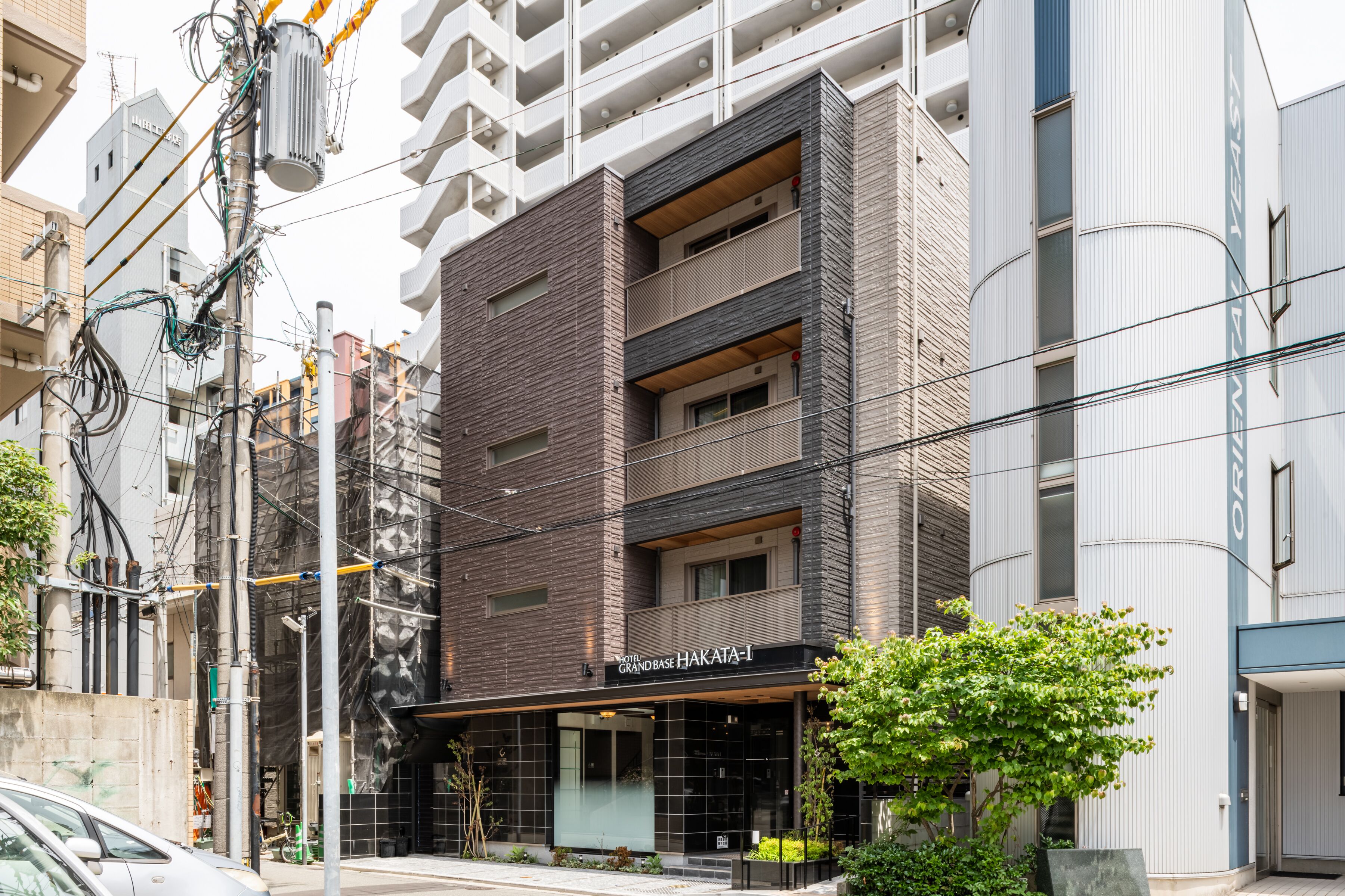A multi-story hotel with a modern facade, featuring a prominent entrance with a glass door and a sign that reads "HOTEL GRANDBASE HAKATA-I".