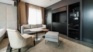 A modern hotel room with a sofa, armchair, ottoman, and a small table. There is a minibar and a TV mounted on the wall. - Grand Base Hakata-Ⅰ (Fukuoka)
