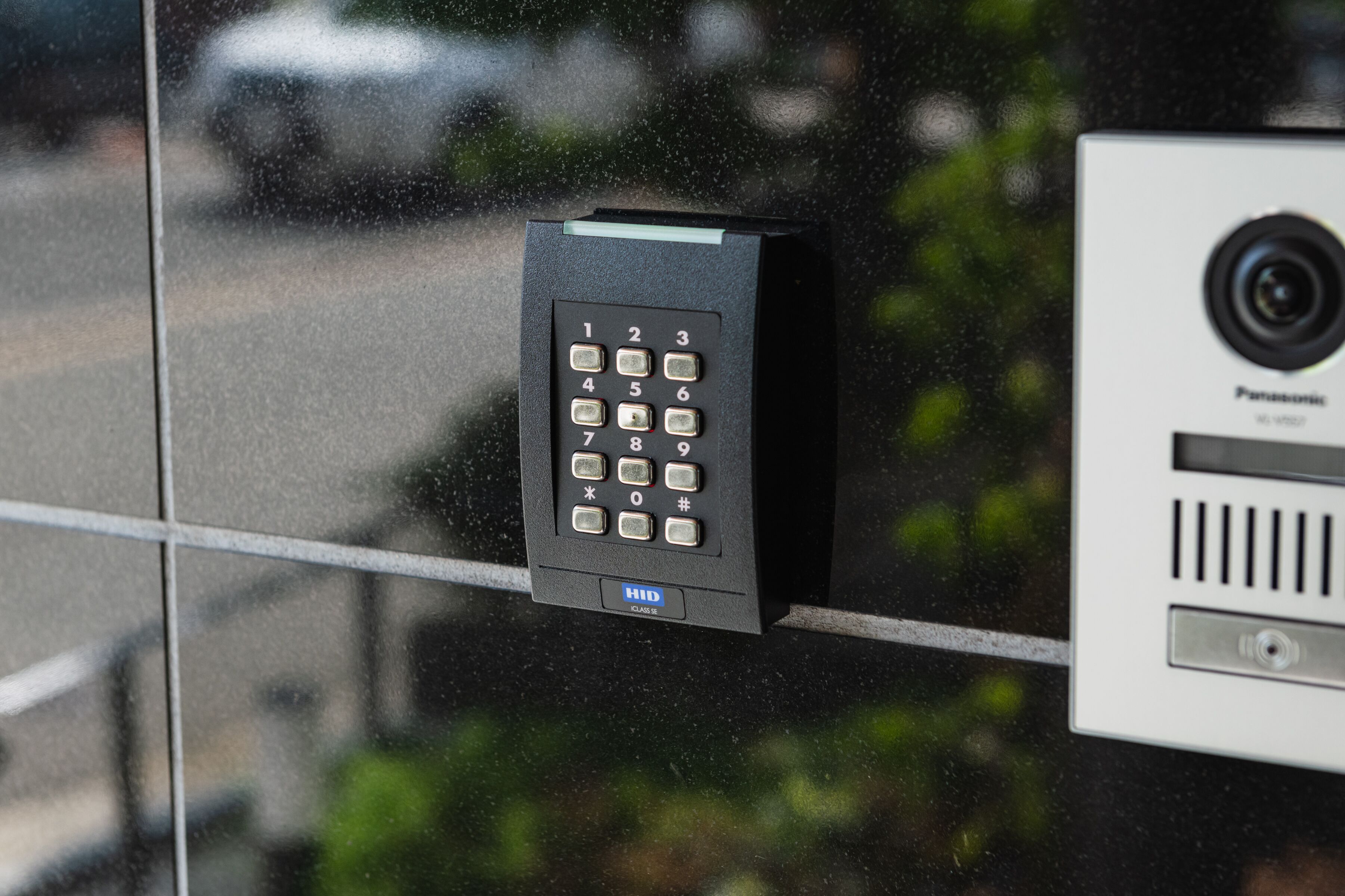 A security keypad and a surveillance camera mounted on a glass door.
