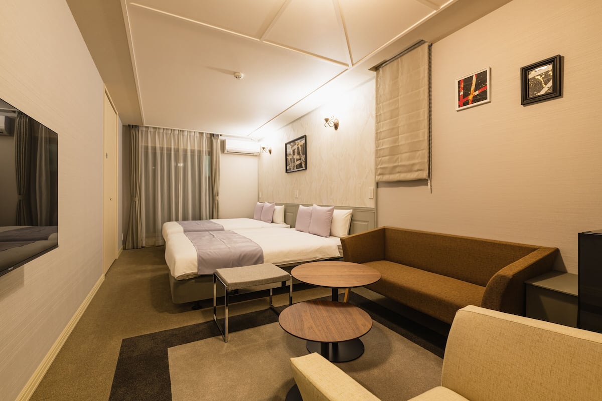 A hotel room with a bed, a sofa, a small table, and a television.
