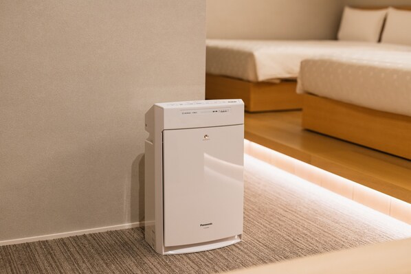 A white Panasonic air purifier in a room with a bed and a wooden floor. - Grand Base Hakata Station (Fukuoka)