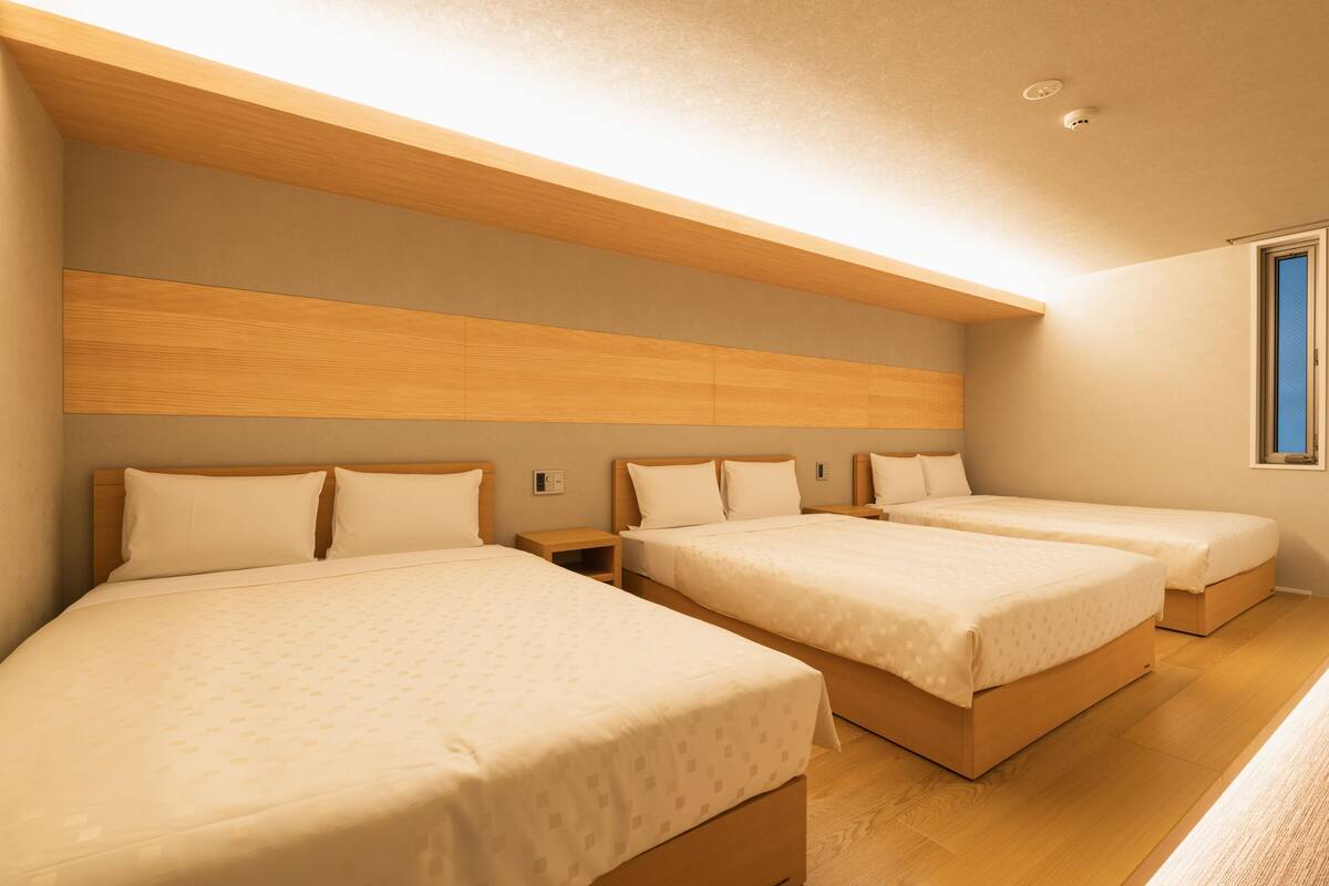 A hotel room with three single beds, wooden headboards, and a large window.