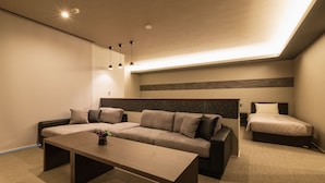 Habitación de hotel moderna con sofá, cama, mesa de centro y una mesita con una planta.