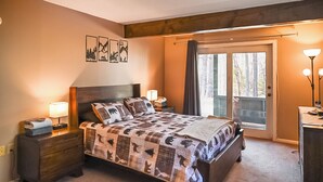 Ein Schlafzimmer mit einem großen Bett, einem Holzkopfteil und Blick auf Bäume durch eine Schiebetür.
