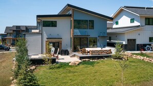 Ett modernt hus i två våningar med en uteplats, utomhusmöbler och en liten trädgård.