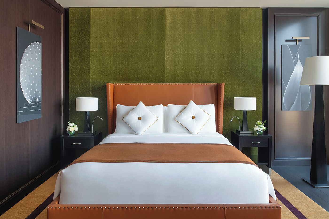 Une chambre d’hôtel avec un grand lit, deux tables de chevet avec des lampes, un mur vert à texture et une œuvre d’art encadrée sur le côté gauche.