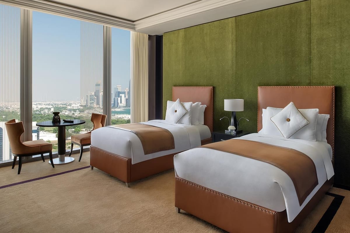 Ein Hotelzimmer mit zwei Betten, einem runden Tisch und Blick auf eine Stadtlandschaft.
