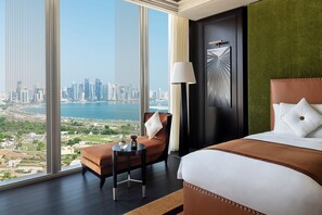 Ein Hotelzimmer mit großem Fenster, einem Bett, einem Sessel, einem Tisch und einer Lampe.