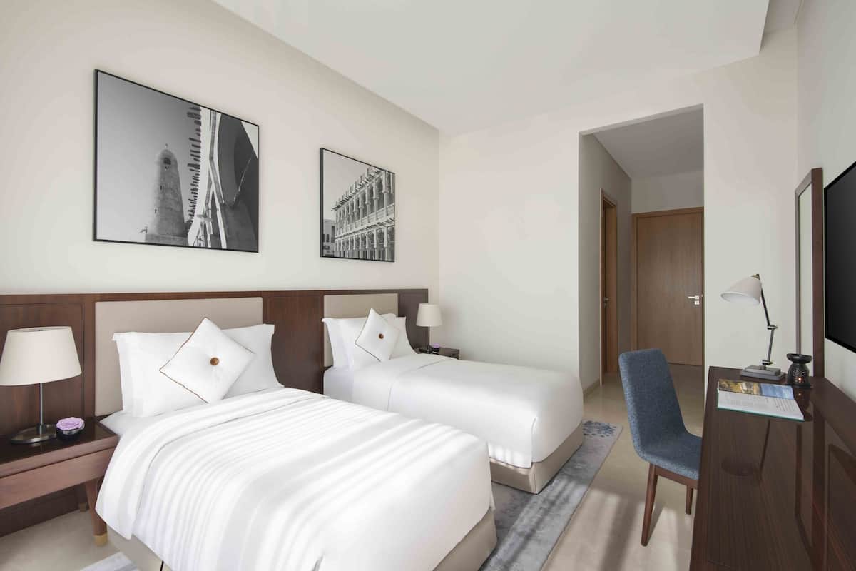 Ein Hotelzimmer mit zwei Betten, einem Schreibtisch mit Stuhl, einem Fernseher und zwei gerahmten Bildern an der Wand.