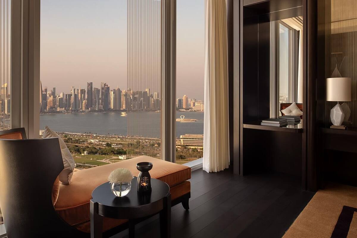 Ein modernes Hotelzimmer mit großem Fenster und Blick auf die Stadt, einer gemütlichen Sitzecke und einem kleinen Tisch mit Dekoration.