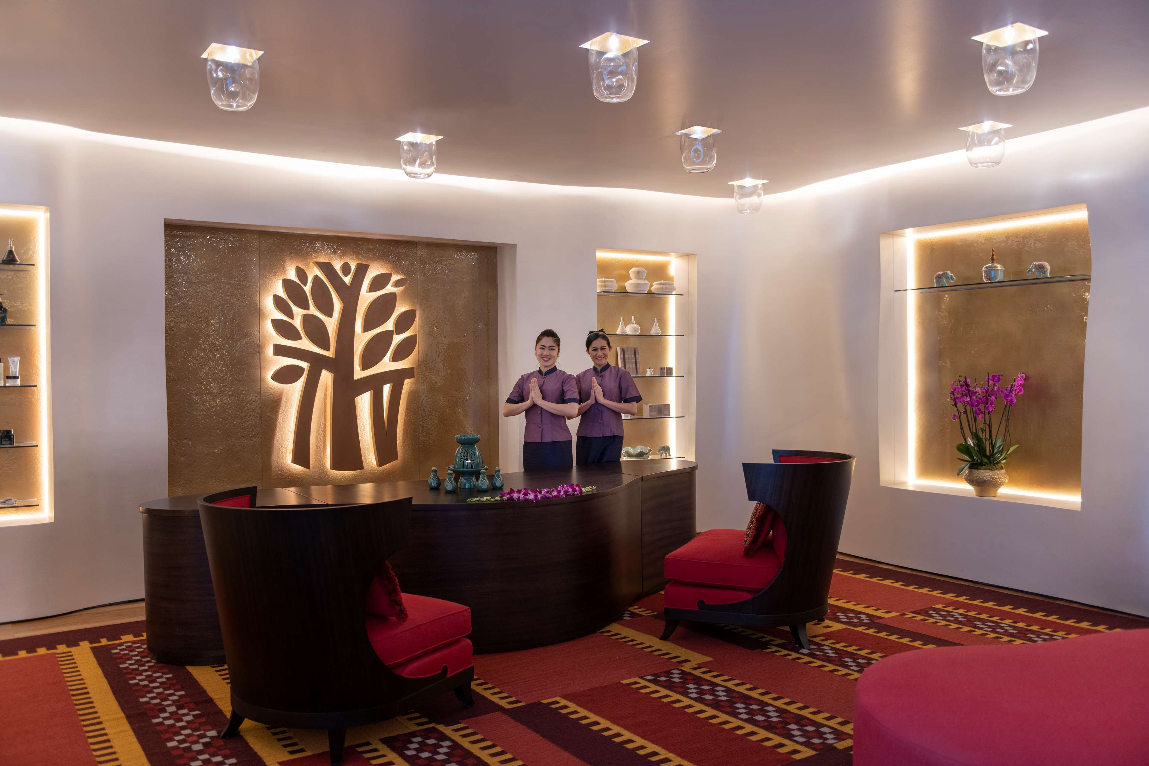 Un espace d’accueil au design moderne, comprenant une grande sculpture d’arbre illuminée, un comptoir d’accueil et un coin salon avec des fauteuils à revêtement rouge.