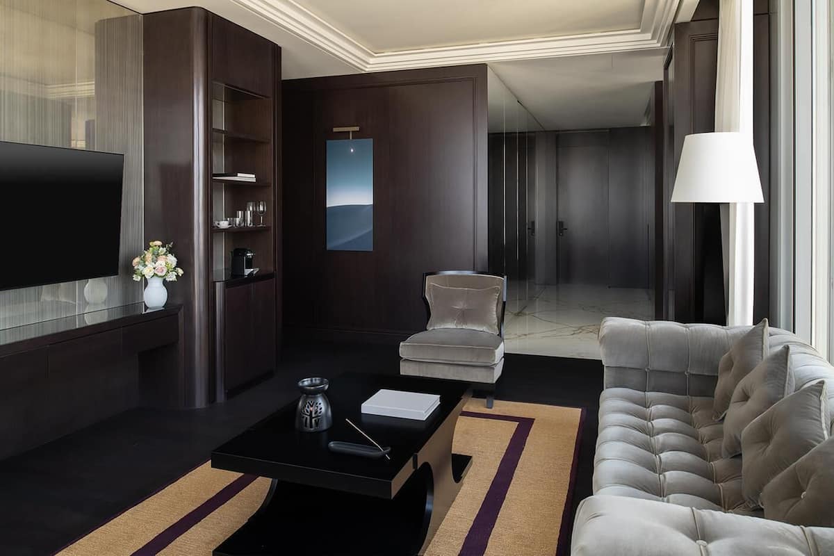 Ein modernes Hotelzimmer mit Flachbildfernseher, einer Couch, einem Sessel, einem Couchtisch und einem großen Fenster.