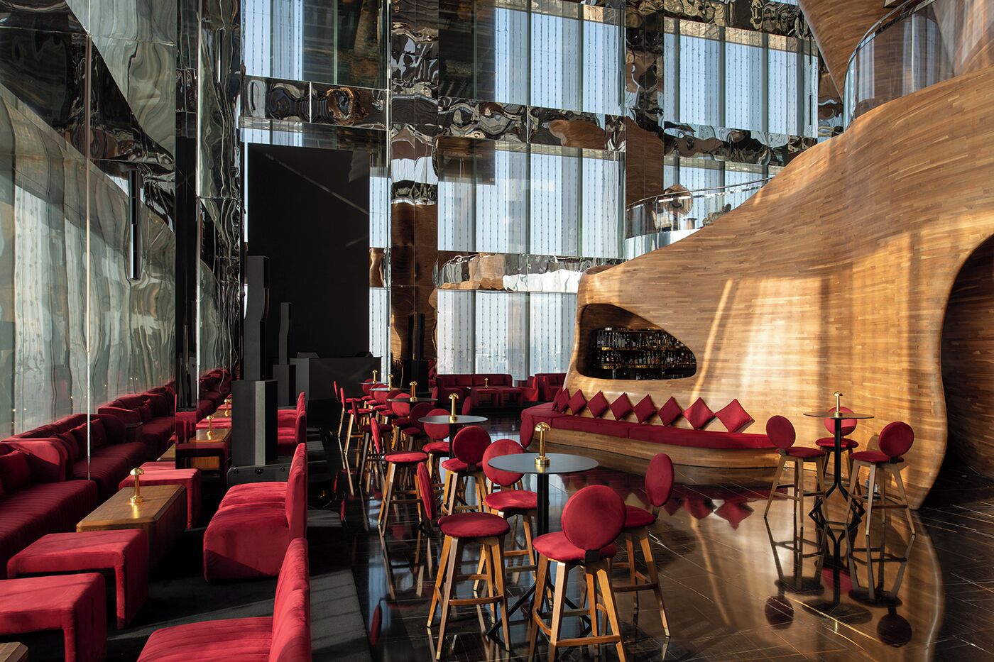 Un interno moderno con un'area bar caratterizzata da una struttura curva in legno e sedute imbottite rosse.