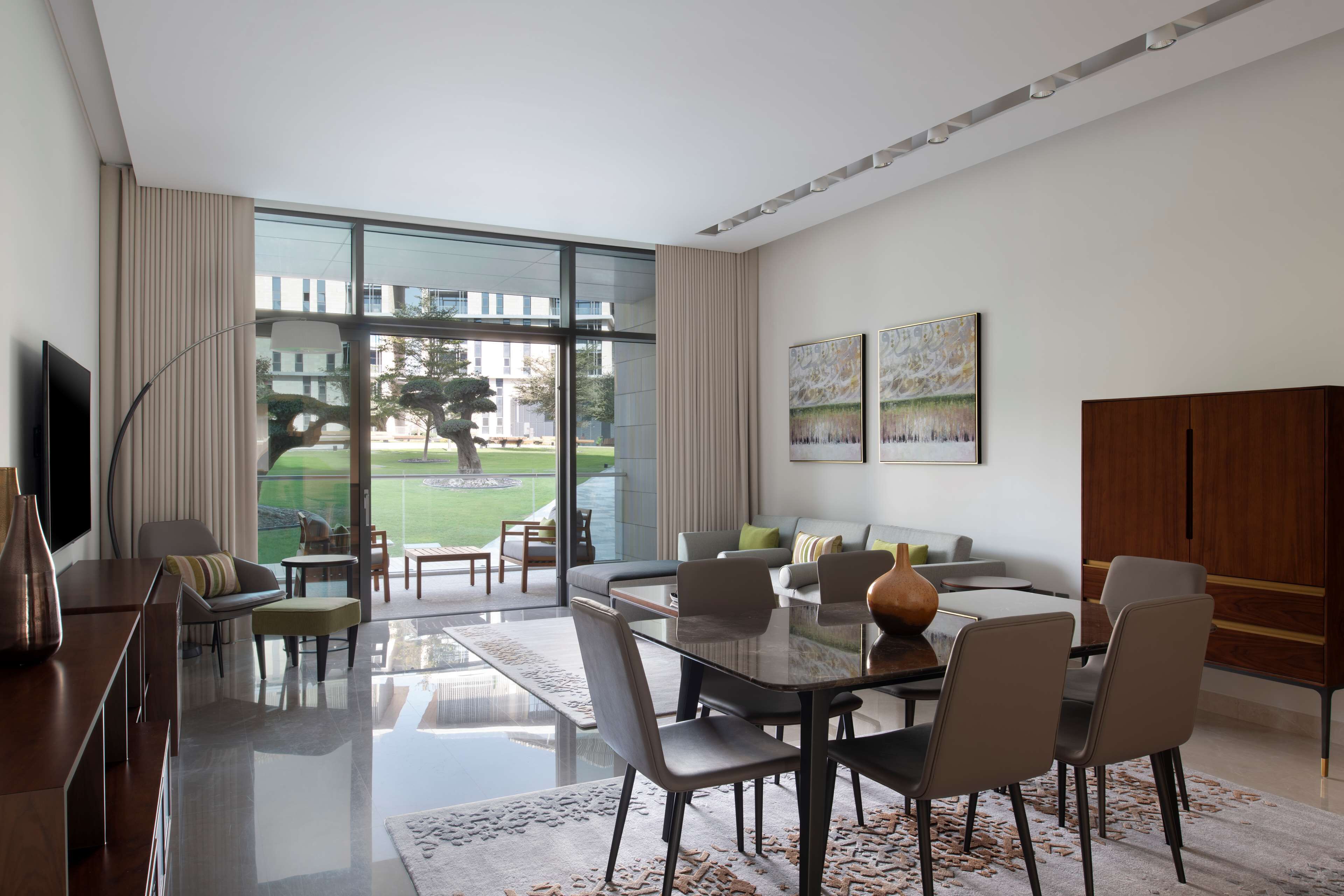 A modern living room with a glass dining table, comfortable seating, and artwork on the walls.