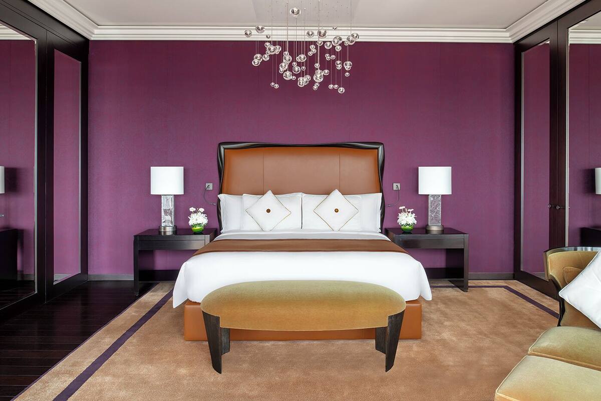 Una habitación de hotel moderna con una cama grande, dos mesitas de noche con lámparas, un candelabro y vistas a la ciudad.