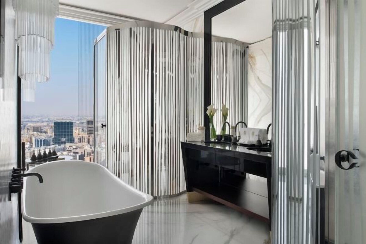 A modern bathroom with a freestanding bathtub, a large mirror, and a city view.