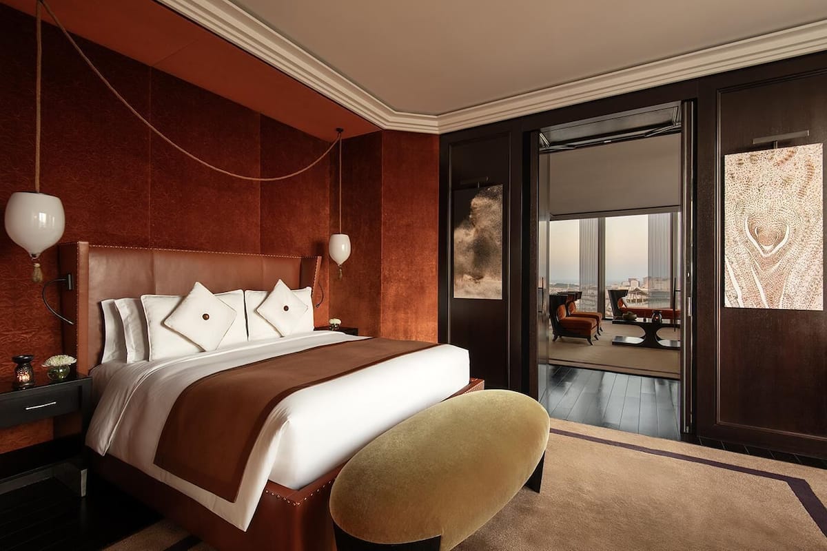 Ein Hotelzimmer mit einem großen Bett, einer Sitzecke mit einem Sessel, Blick auf die Stadt durch ein großes Fenster und einem modernen Design.