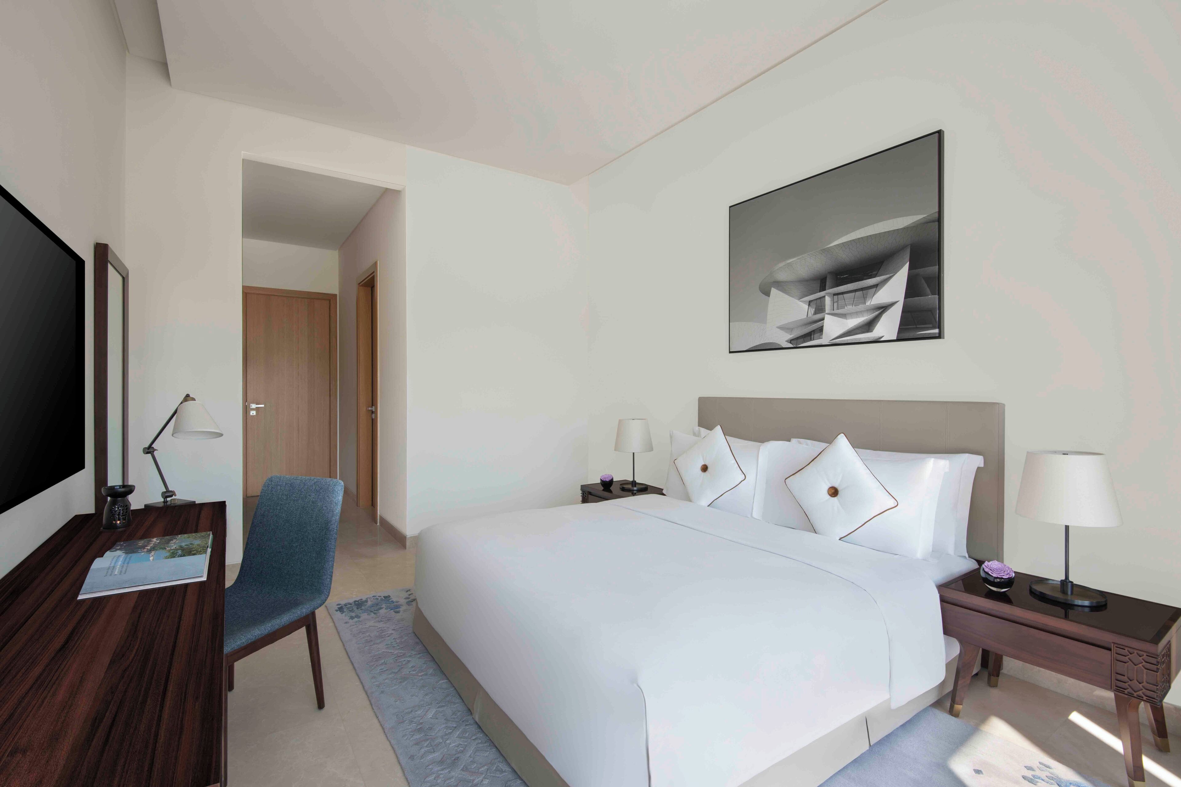A hotel room with a large bed, a desk, a chair, a TV, and a painting on the wall.