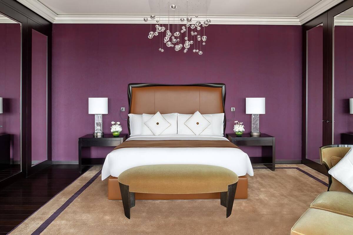 Ein modernes Hotelzimmer mit einem großen Bett, zwei Nachttischen mit Lampen, einer Chandelüster und Blick auf die Stadt.