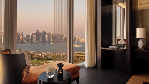A modern hotel room with a large window offering a city view, a comfortable seating area, and a small table with decorative items. - Banyan Tree Doha at La Cigale Mushaireb (Doha)