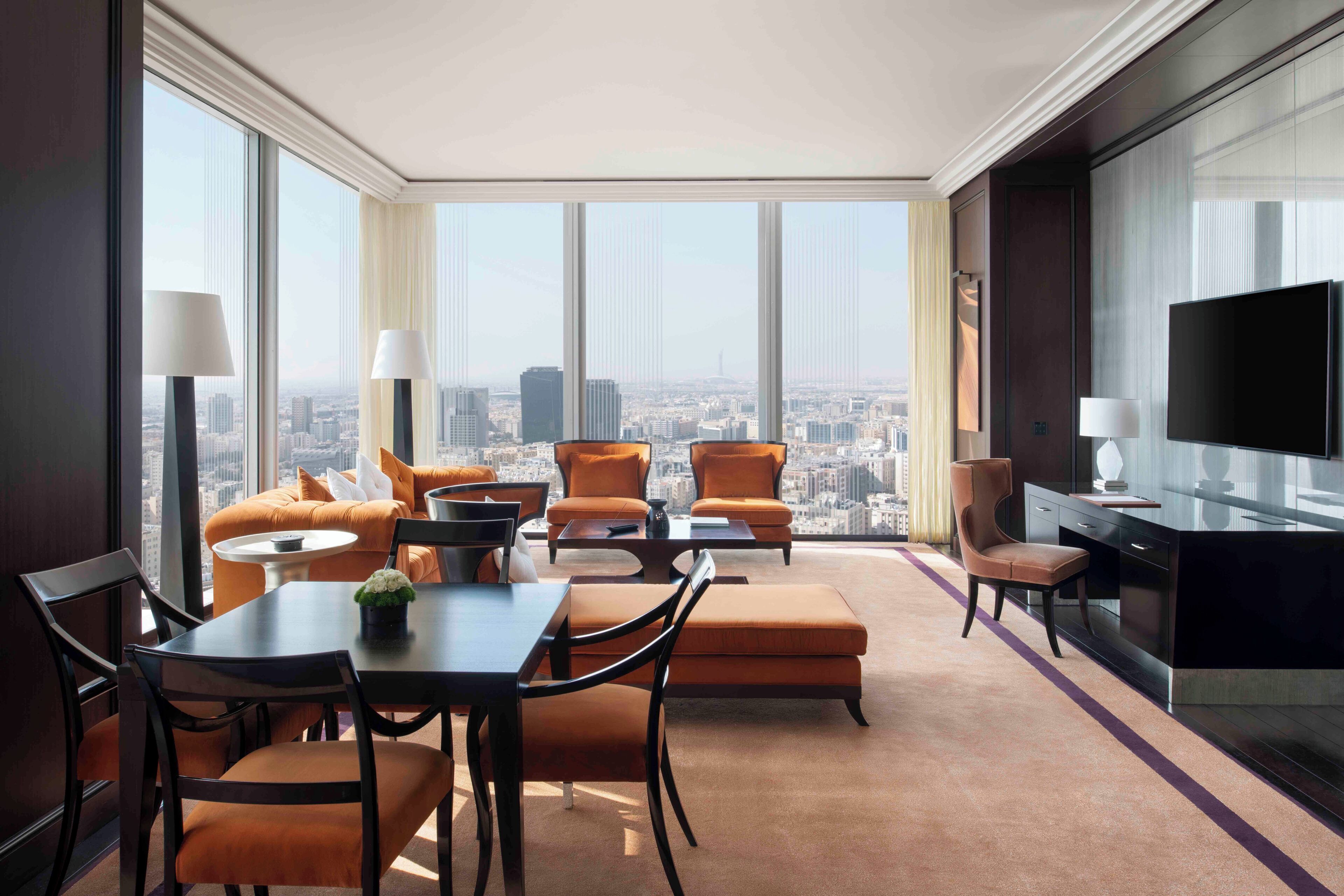 A modern hotel room with a city view, a dining area, and a flat-screen TV.