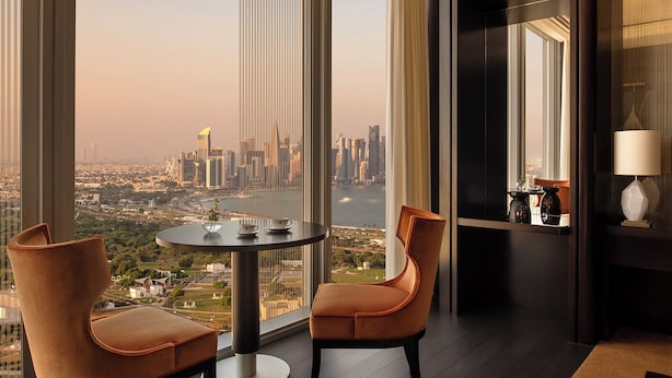 A high-rise room with a city view, a round table, two chairs, and a lamp.