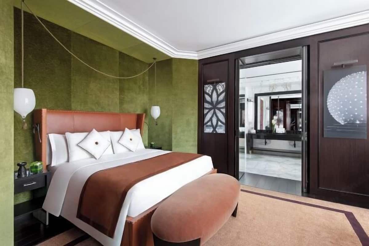 Ein modernes Hotelzimmer mit einem großen Bett, einer Bank, einem Nachttisch und Blick durch eine Glastür.