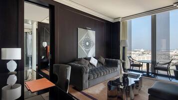 Habitación de hotel moderna con pared de madera oscura, un ventanal con vista a la ciudad, un sofá gris con cojines, una mesita redonda y una mesa de centro de vidrio.